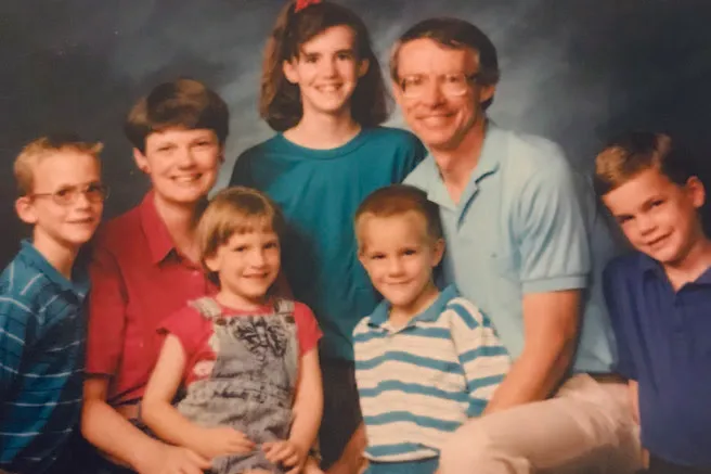 Un retrato familiar alegre que presenta a dos padres y sus cinco hijos, todos sonriendo cálidamente contra un fondo azul